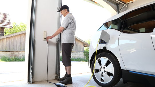 Mann lädt Elektroauto an Schuko-Steckdose in Garage